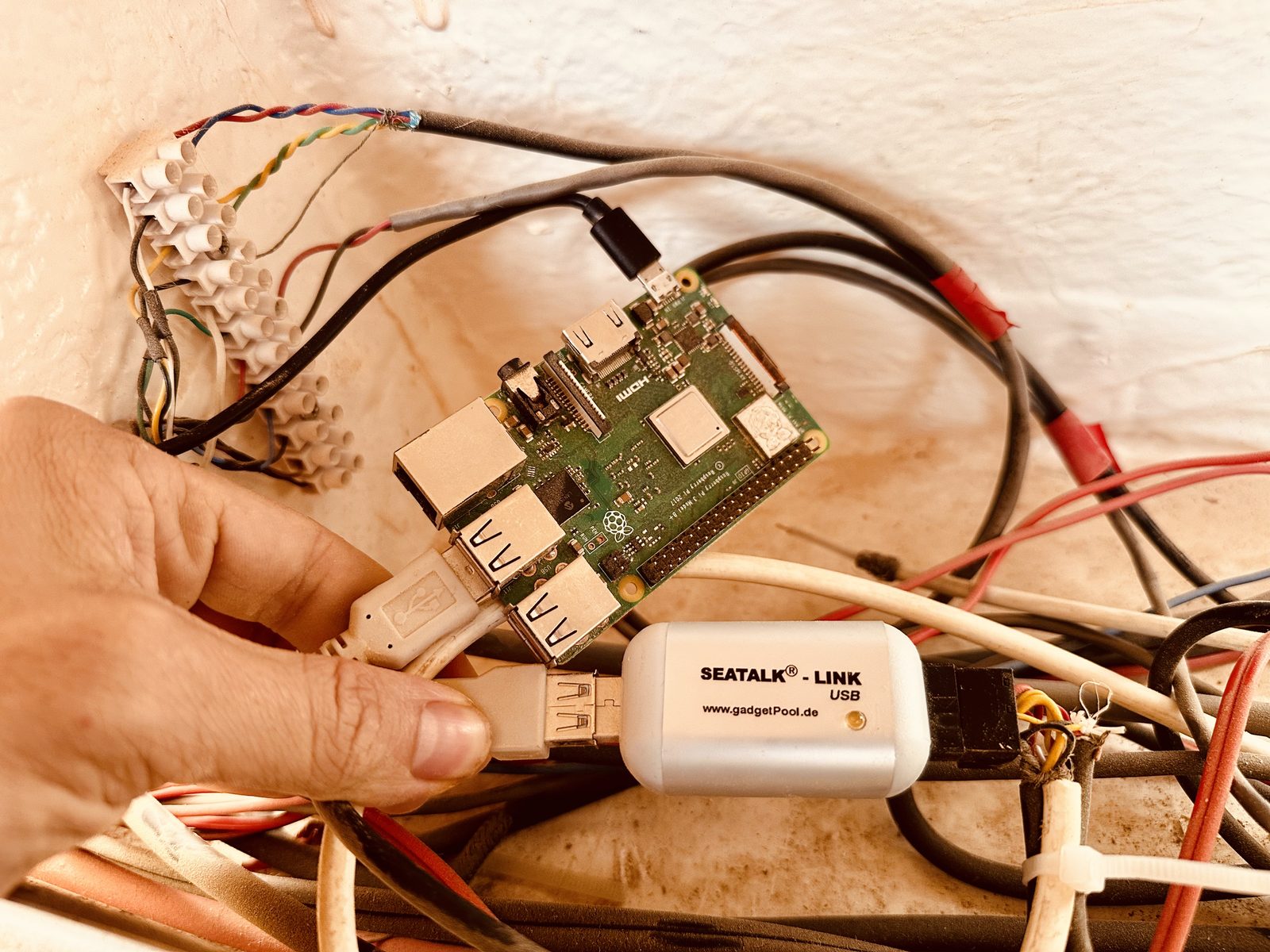 Raspberry Pi 3+ and white SEATALK-LINK USB bridge from gadgetPool.de, held next to a tangle of boat wiring
