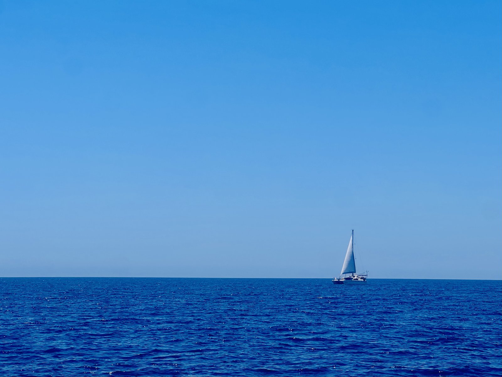 A distant catamaran on a calm blue sea, sailing on the Aegean
