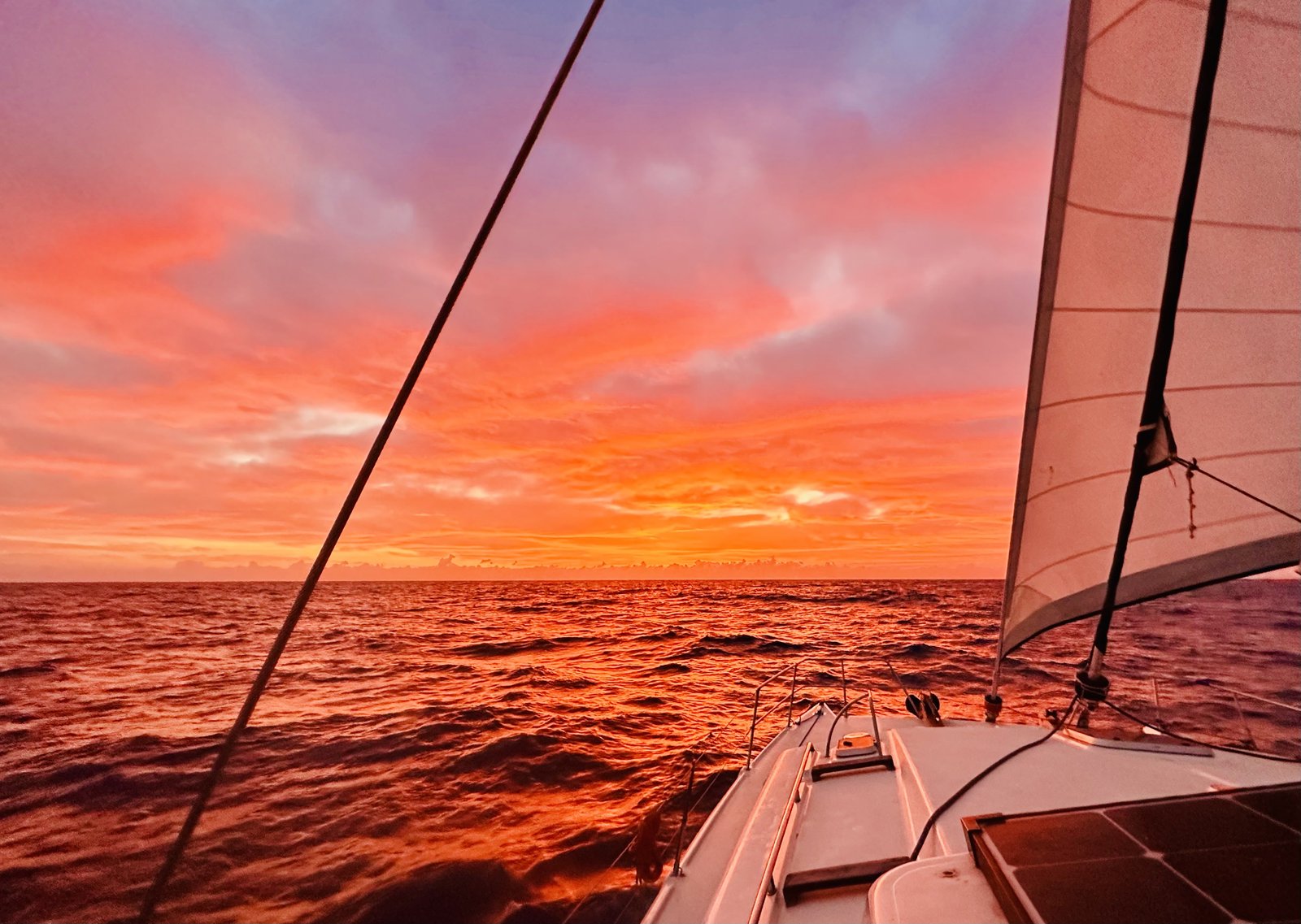 Sunset over the Aegean from the deck of the catamaran, sail and rigging silhouetted against an orange sky